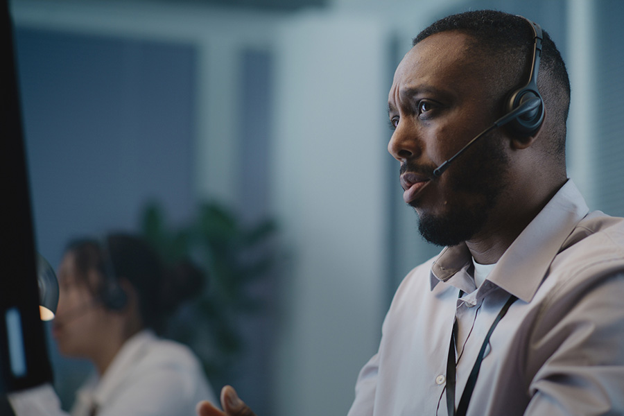 A man with a headset answers calls on the 988 lifeline while looking at a computer screen and chatting with a caller