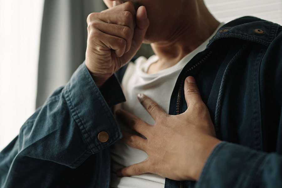 A person coughing and holding their chest during allergy season