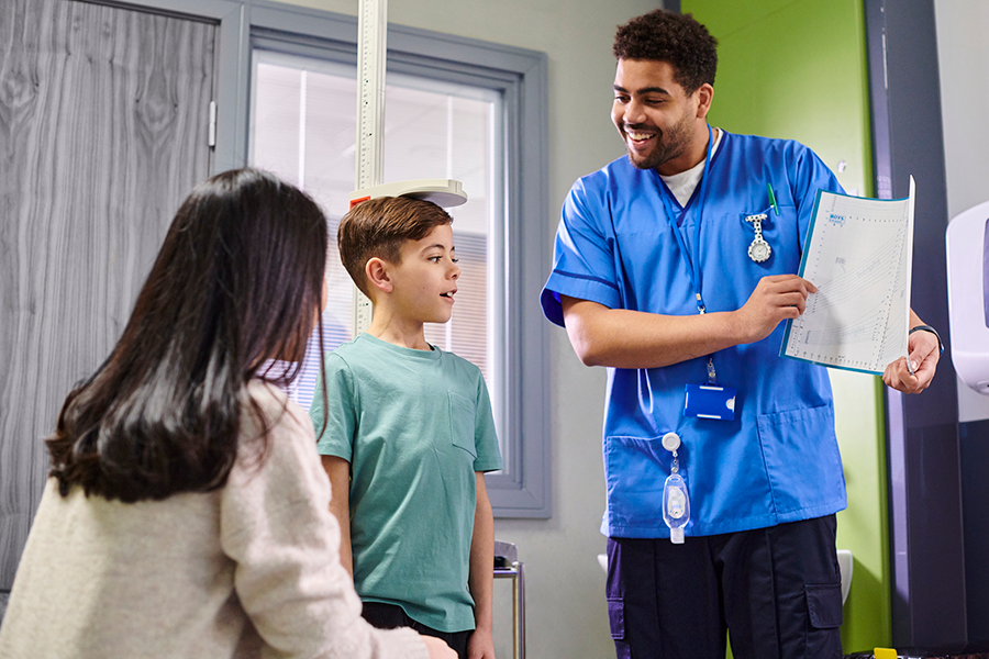 A pediatrician measures a child's height for an annual physical while the child's mother looks on