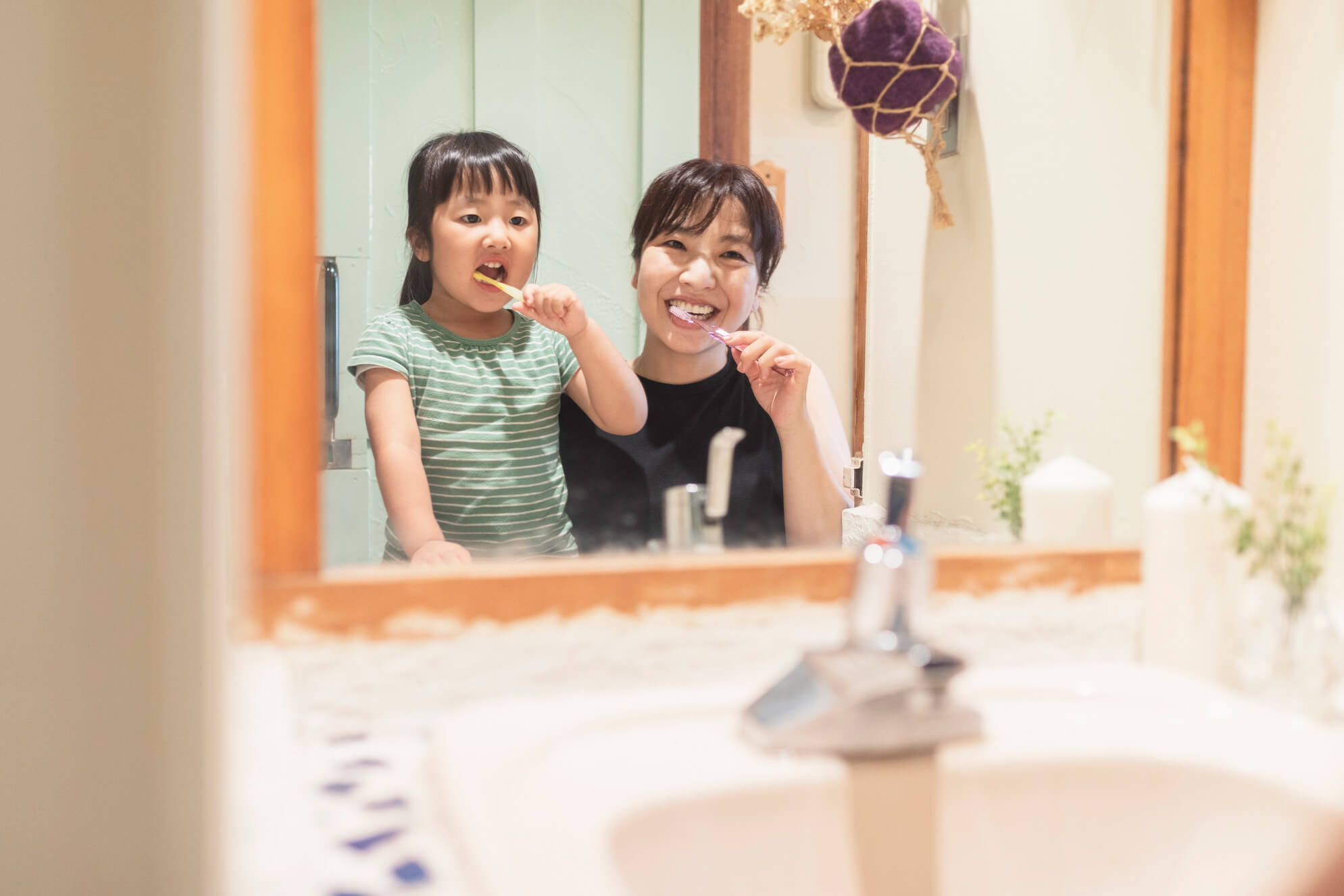 Young child practicing brushing with their mother while looking in the mirror