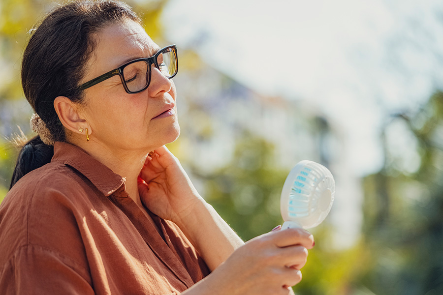 A woman standing outside uses a portable fan to cool herself down during the heat of the summer