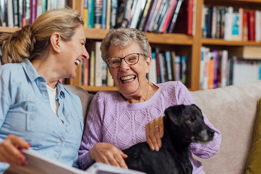 Elderly woman with a gentle smile sitting beside a supportive caregiver at home