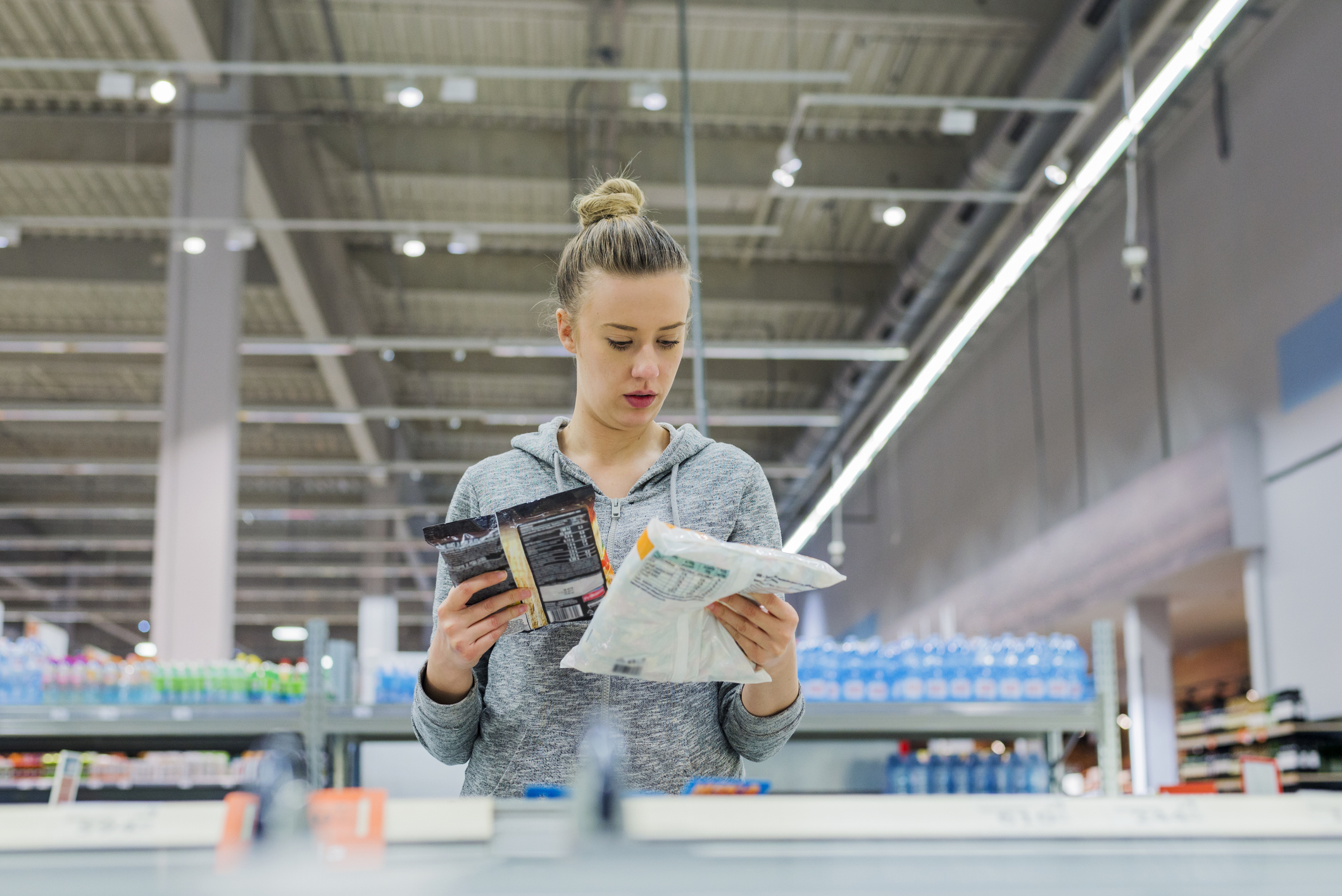 Pregnant Woman buying frozen food and holding a deep-frozen product in a supermarket, I always check the ingredients. Cheerful young female holding food from refrigerator while standing in a food store