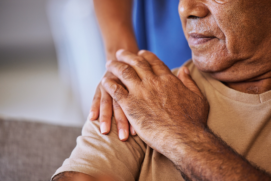 An elderly man touches the hand of another person's comforting hand