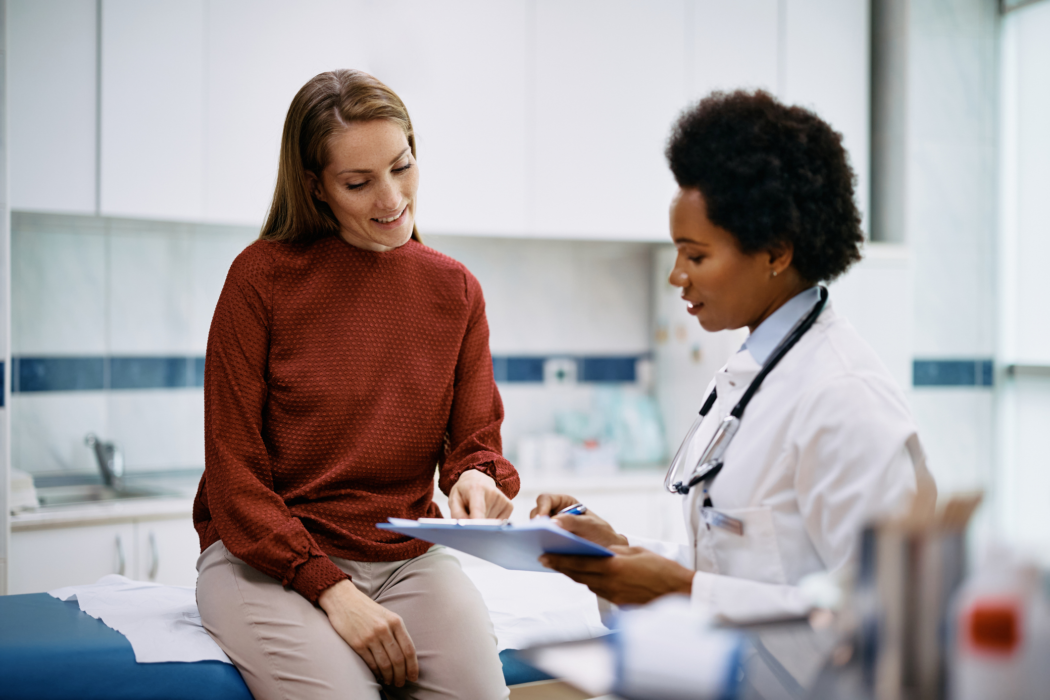 African American doctor and her female patient analyzing medical report after examination in the hospital. Focus is on female patient. 