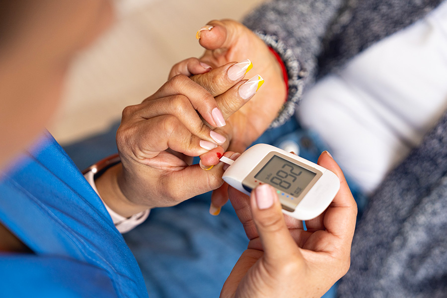 A clinician holds a glucose monitor against a patient's finger to collect their blood for monitoring their blood sugar level