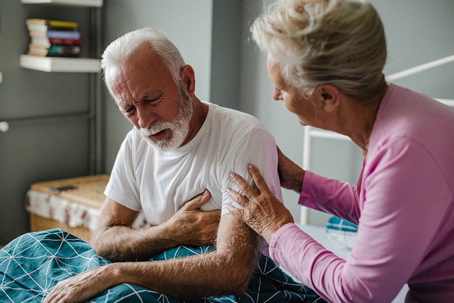 An elderly woman checks on her husband, who is grabbing his chest due to a heart attack, a common risk factor for stroke