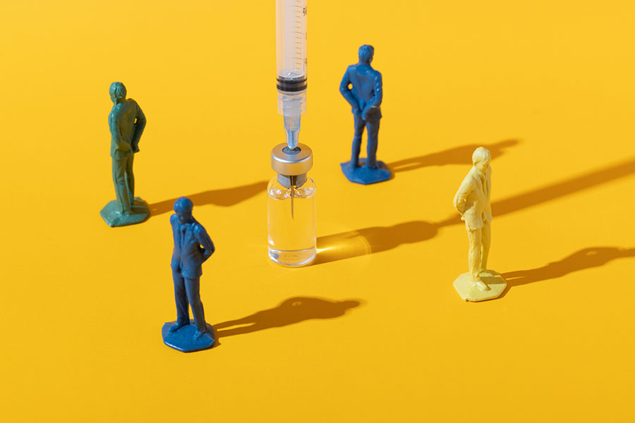 Figurines of people stand facing away from a vaccine, signifying their resistance to vaccination